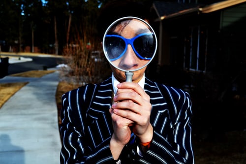 Man holding a magnifying glass in front of his face to demonstrating how to search for hashtags on TikTok.