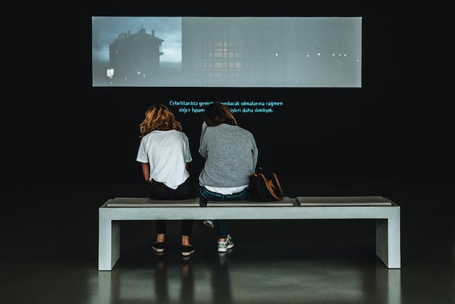 Two people watching a video on a big screen with captions.