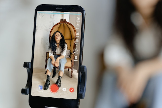 A close-up of a woman sitting on a chair, recording a Tik Tok video.