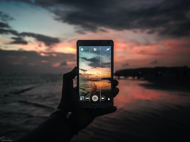 A phone screen displaying a camera grid with the beach at sunset in the background.