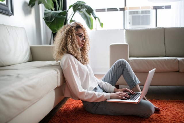 A woman sitting on the floor typing comments on her laptop.