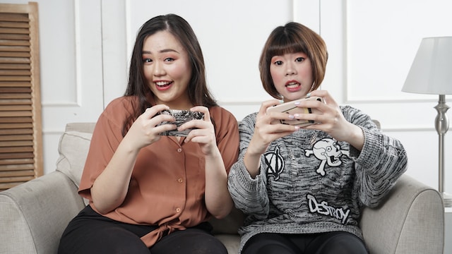 Two women using their phones and sharing a couch.