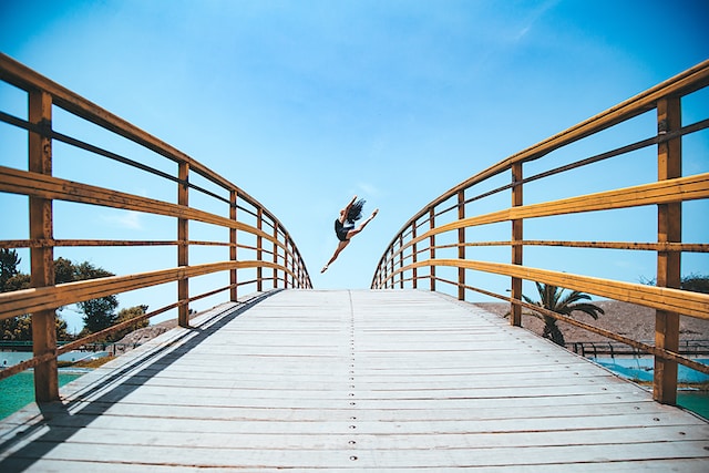 A woman leaping for a dance on a bridge.