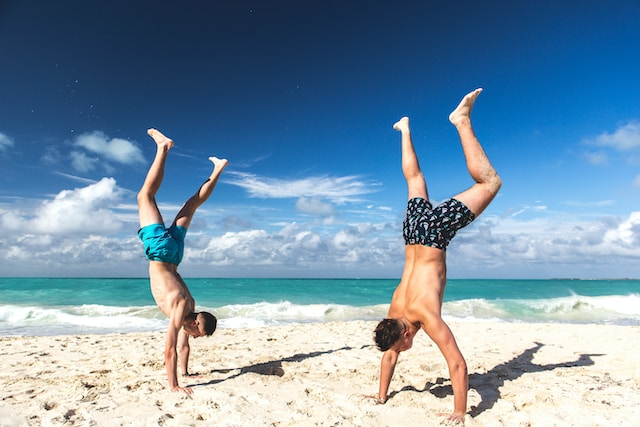 Two men doing handstands at the beach.