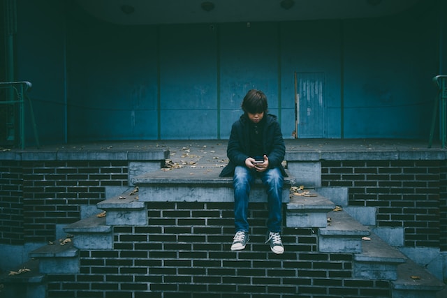 A boy sitting on the steps of an old building while using his phone.