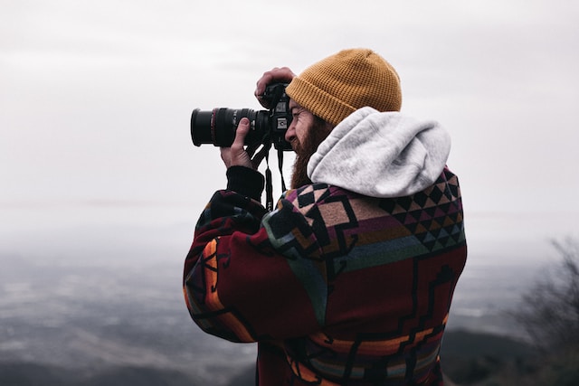 A man on a mountain taking photos with his DSLR camera.