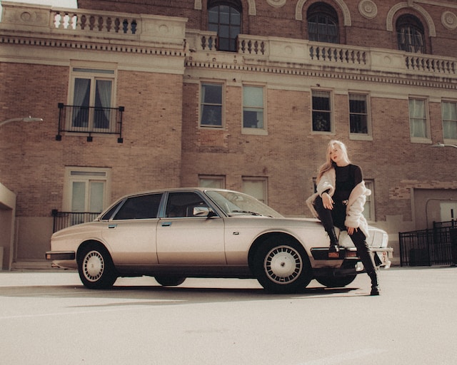 A female model sitting on the hood of a car.