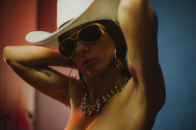 A woman wearing a cowboy hat, sunglasses, big earrings, and a heavy chain necklace.