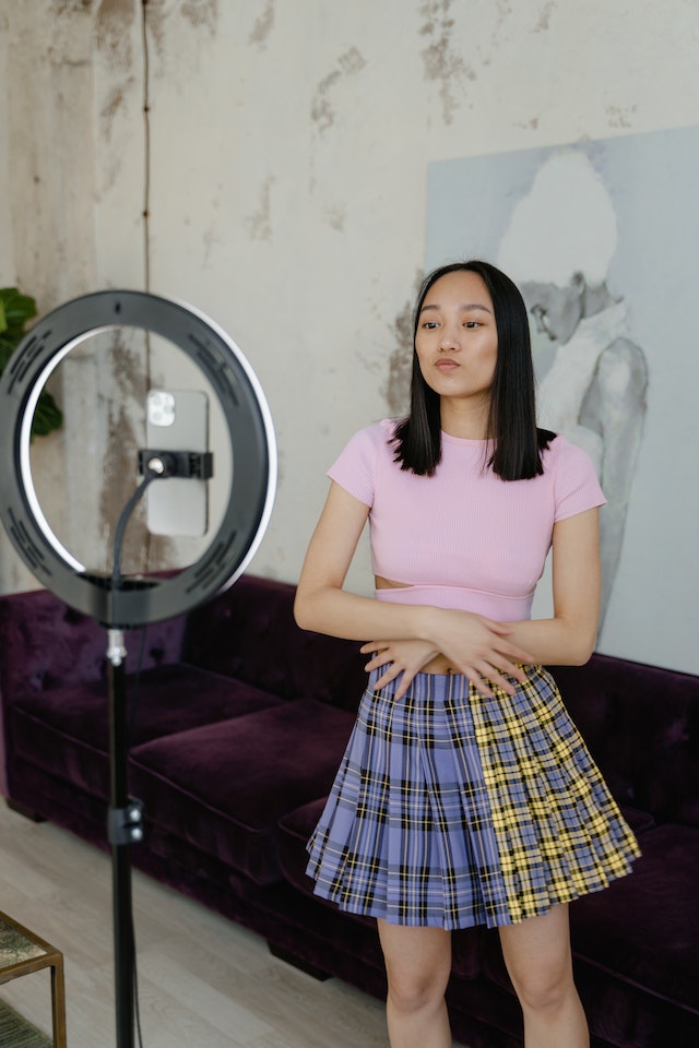 A girl standing and recording a video of herself for TikTok.