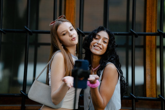 Two smiling young ladies taking a picture with a smartphone.