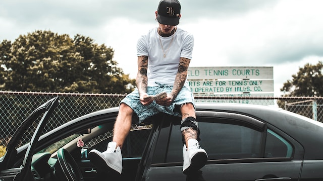 A man sitting on top of a car while counting money.