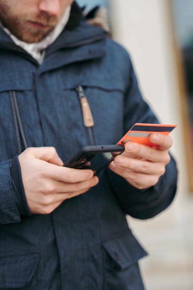 Man holding phone in one hand and a credit card in the other to buy tiktok views.
