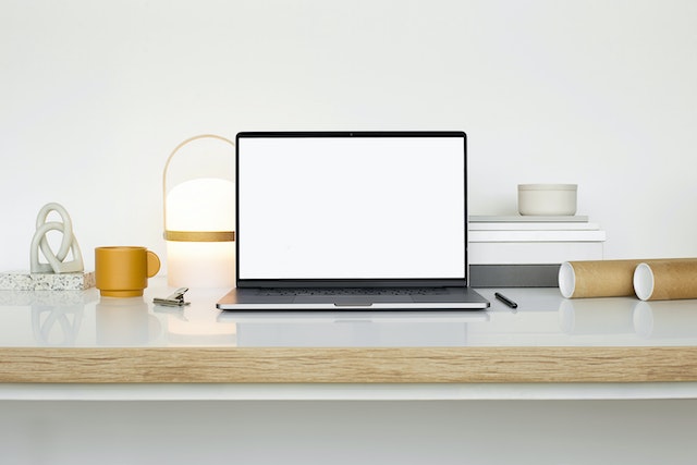 A MacBook, pen, and cup on a white surface.