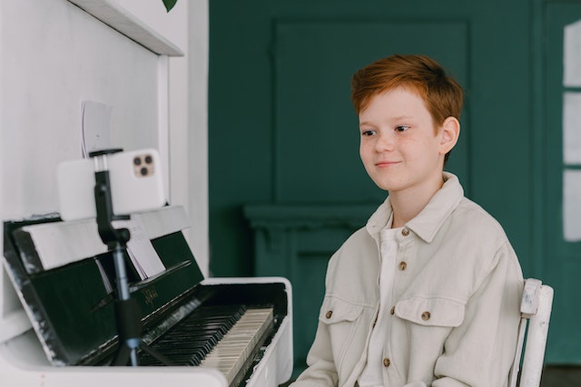 A kid recording a video of himself for TikTok playing the piano.