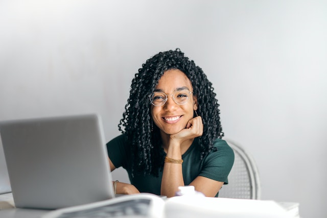 A young influencer sitting and smiling while creating content on her PC.