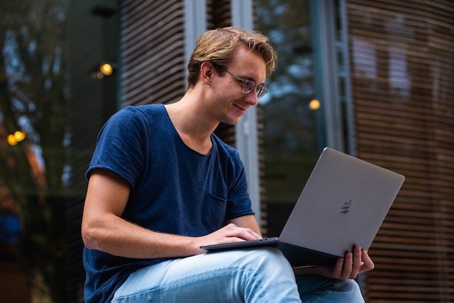 A male tech influencer sitting outside while creating content for his audience on his PC.