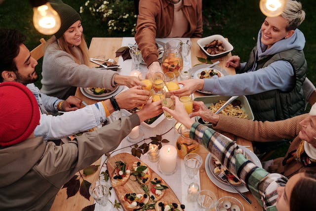 Friends share a toast with their drinks over a table filled with Thanksgiving food.