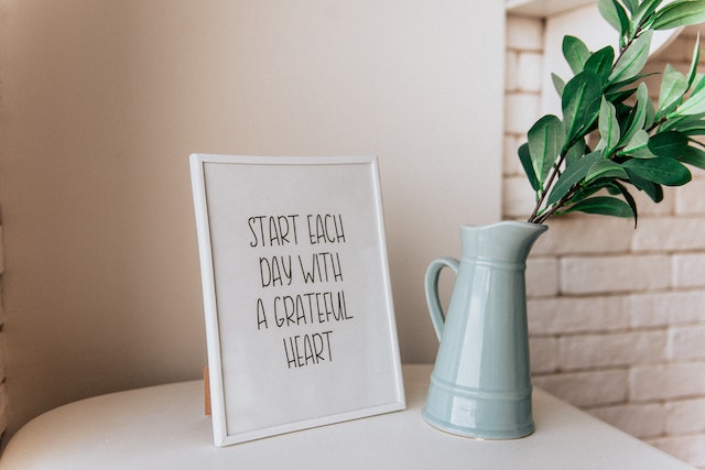 A framed quote sits on a table beside a vase.