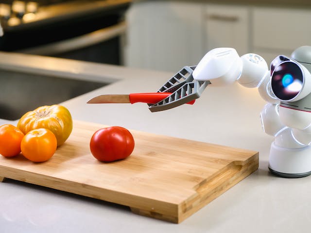 A photo of a small bot holding a tiny knife over some tomatoes.