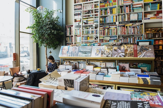 A woman sits at a bookstore table while watching videos on her phone.