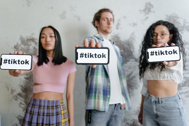 A picture of three people holding up their phones to show “#tiktok” on the screens.