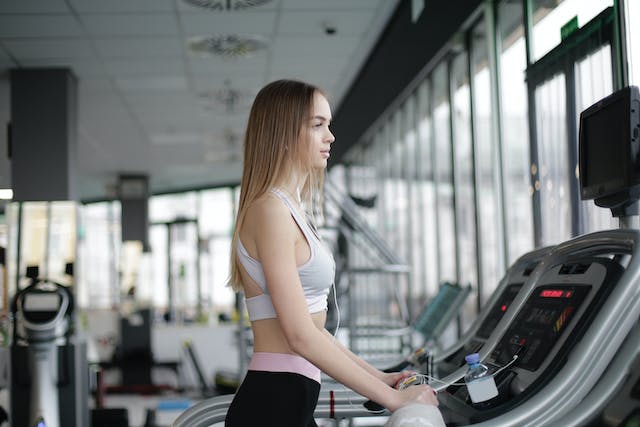 A photo of a woman standing on a treadmill.