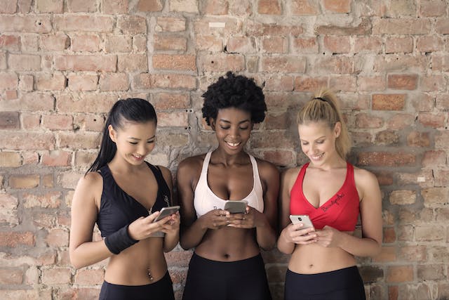 Three women in sportswear browse online on their phones.