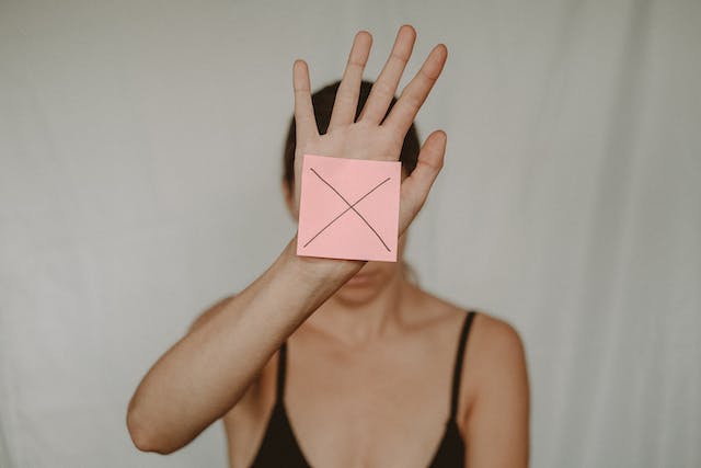 A photo of a woman showing a post-it on her hand with the letter X printed on it.