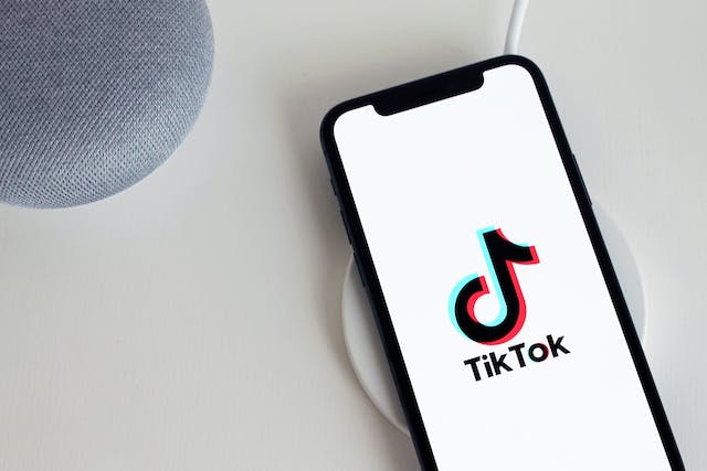 A white phone screen displays the TikTok logo and name as the app loads.