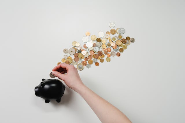 A person puts coins in a black piggy bank.