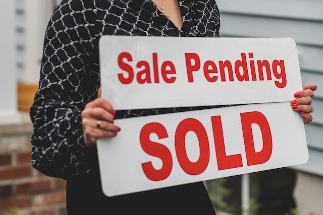 A person holds a sign that reads “Sale pending” and “Sold.”