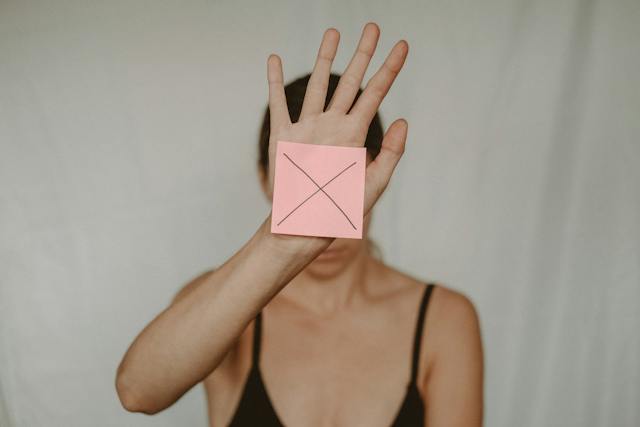 A woman holds up her hand with a Post-it note showing the letter X.