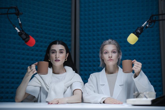 Two women sit in front of microphones inside a sound-proofed studio.