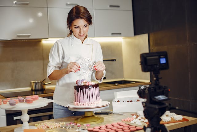 A woman films herself while she decorates a cake.