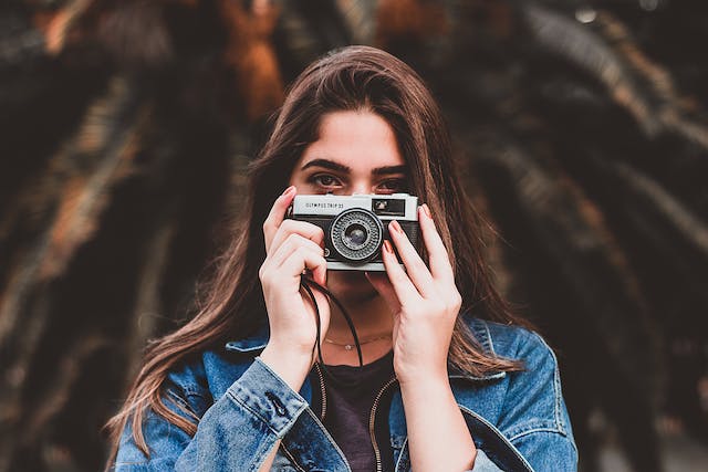 A woman holds a camera in front of her face.