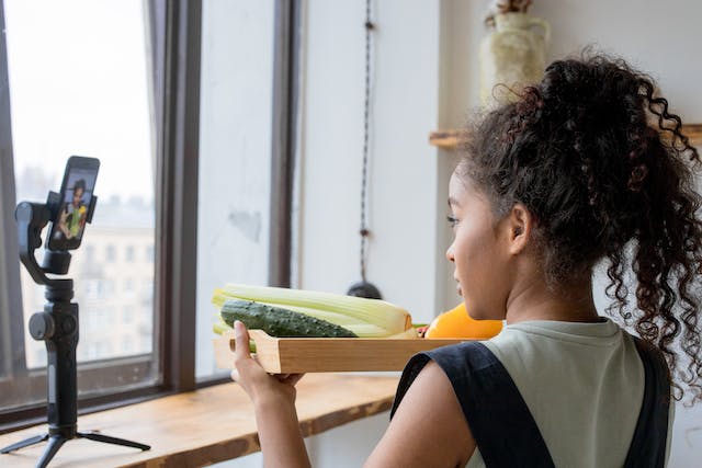 A young woman holds up a tray of fresh vegetables for her TikTok video.