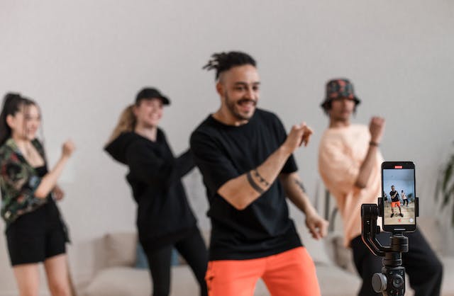 A photograph of people recording a dance video using a mobile device and a phone stand.