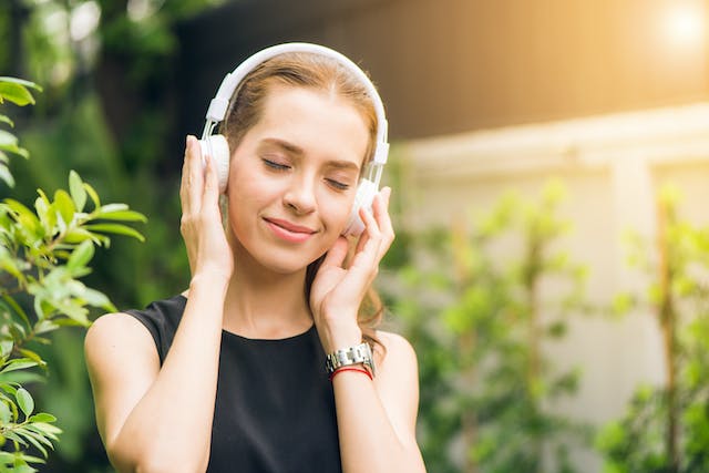 A woman smiles while wearing headphones and listening to music.