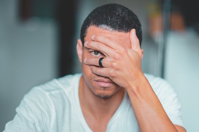 A man covers his face with one hand and peeks in between his fingers.