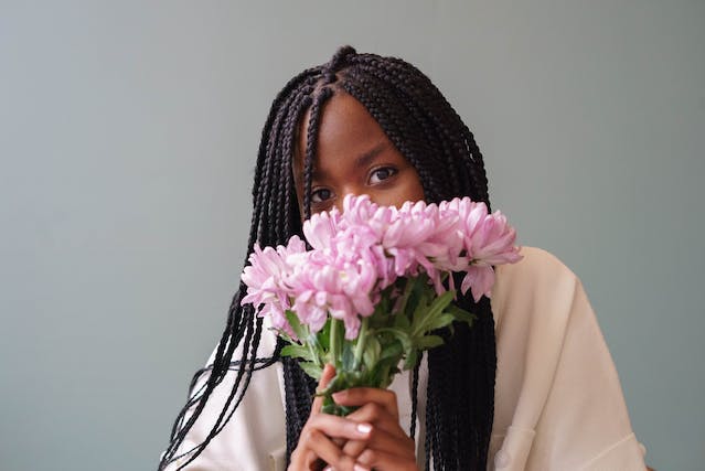 A woman covers the bottom half of her face with a bouquet of pink flowers.