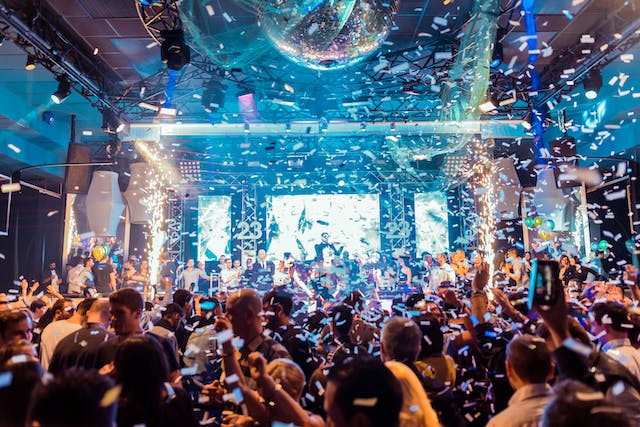 Confetti falls over a big crowd cheering performers on a stage.