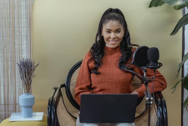 A smiling woman sitting on a chair with a laptop open on her lap.