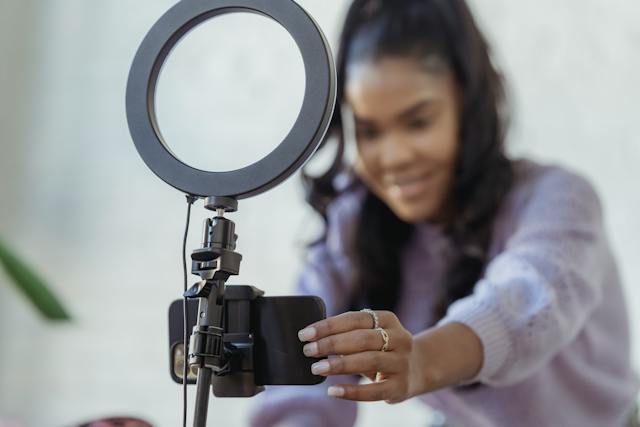 A creator presses a button on her smartphone set up on a tripod.