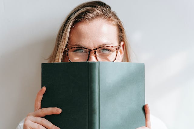 A woman wearing glasses peeks over a book.