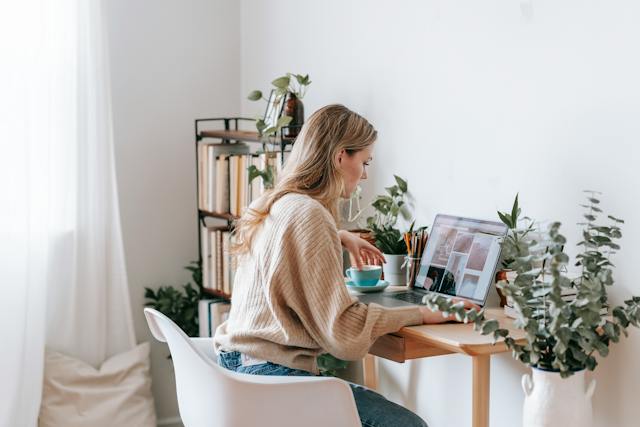 A woman is sitting at a desk and editing images on her laptop.