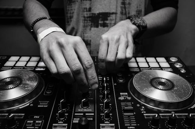 A close-up image of a DJ’s hands playing with the controls of audio equipment.