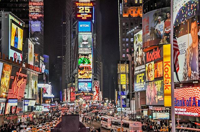 A bustling city street with bright digital billboards at night.