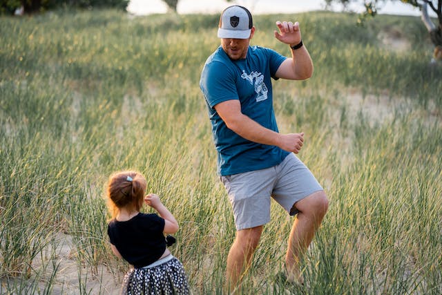 An image of a father and his young daughter dancing in a meadow.
