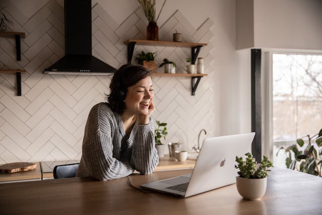 A woman wearing headphones laughs while watching TikTok videos on her laptop.