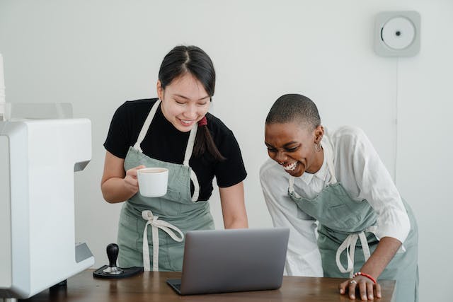 Two female baristas watch videos on a laptop during break time.